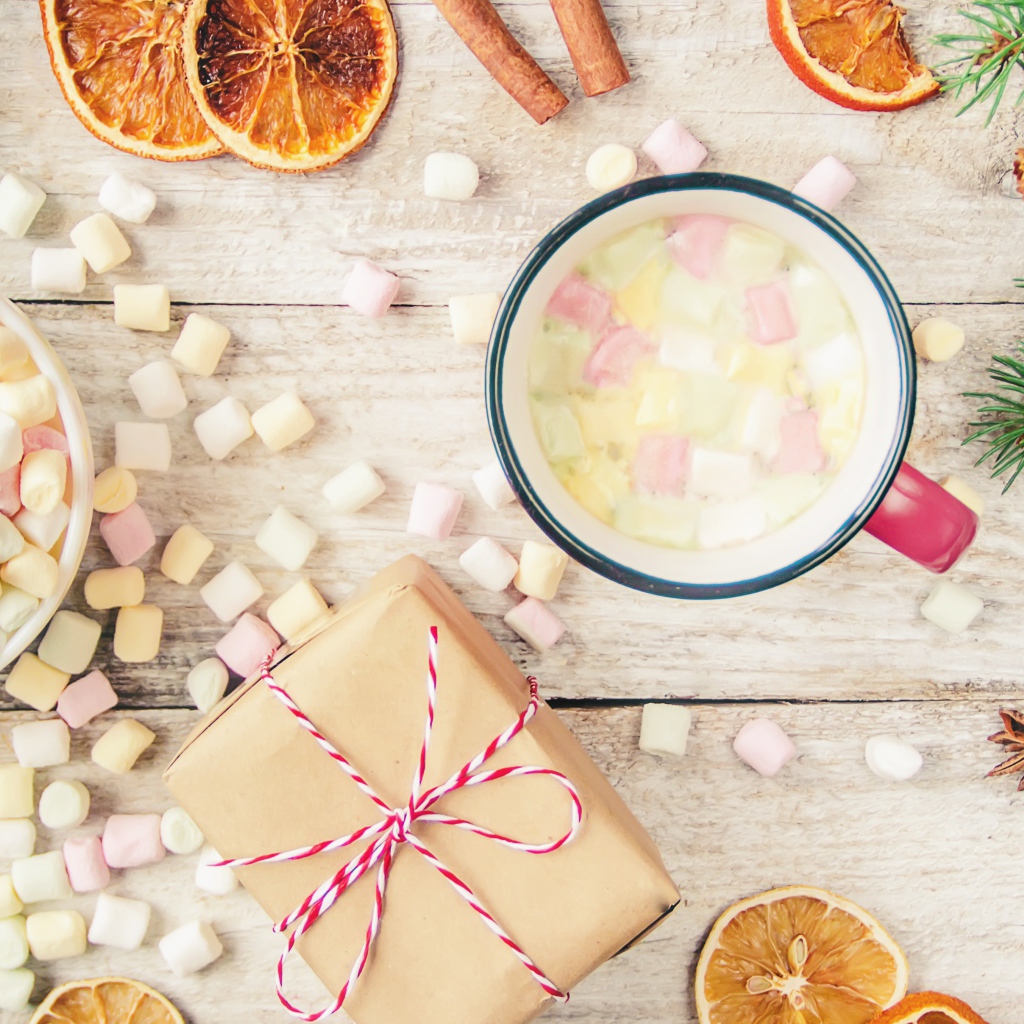 Кружка горячего напитка на столе с маршмеллоу, пряностями и подарком