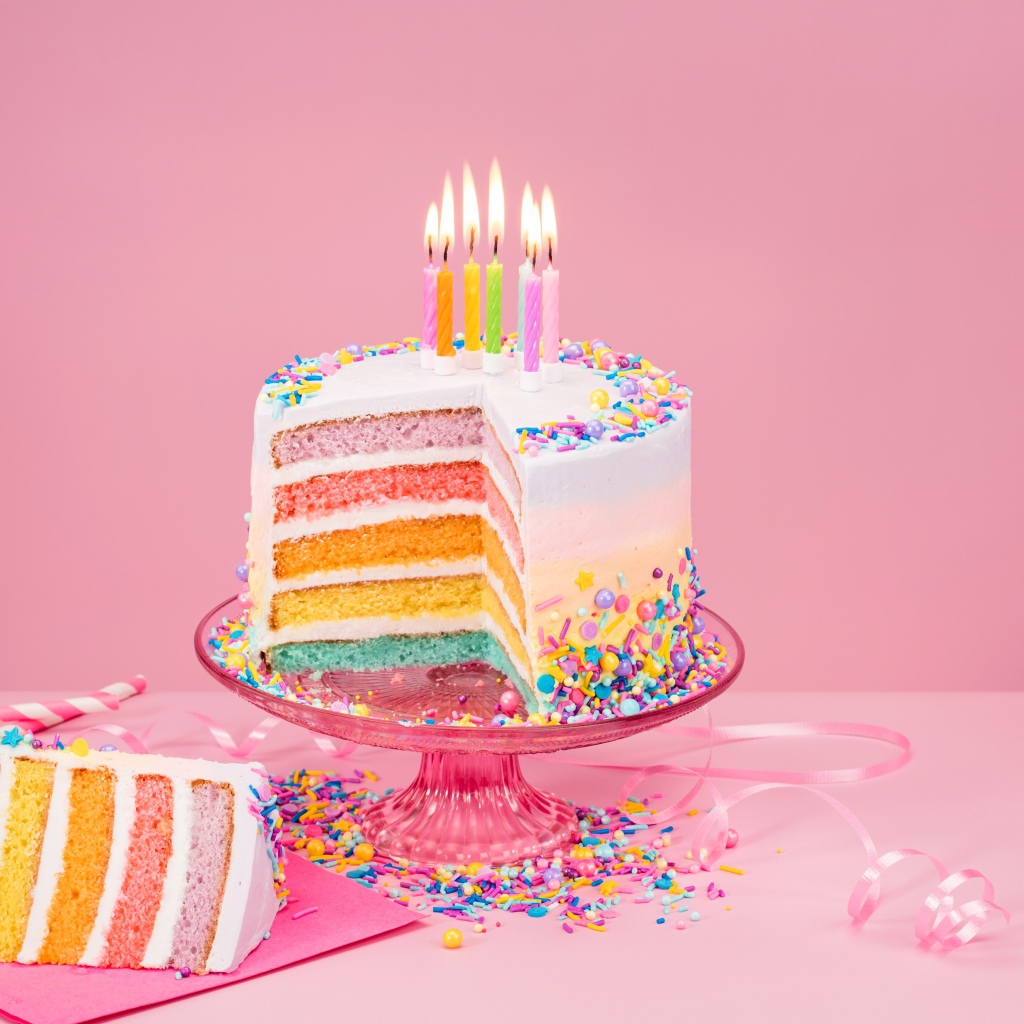 Разноцветный праздничный торт со свечами на розовом фоне
