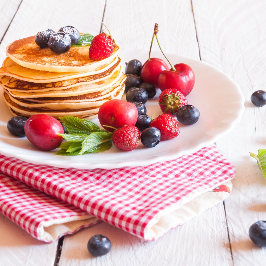 Оладья на белой тарелке с ягодами черники, черешни и клубники