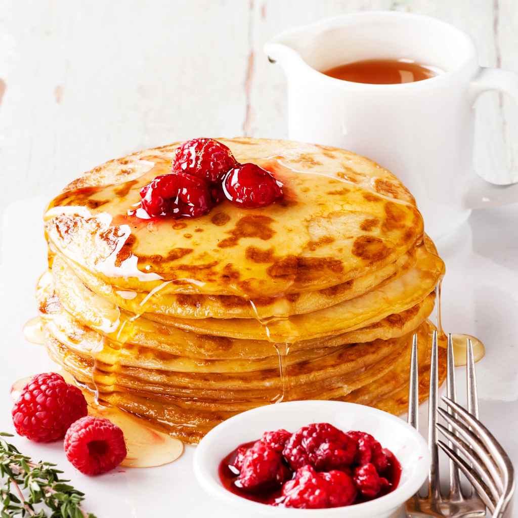 Панкейки с медом и ягодами малины на столе с чаем