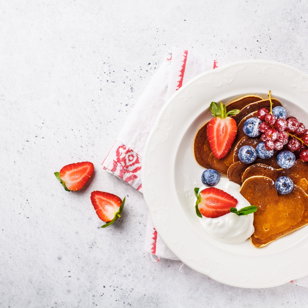 Оладьи со сметаной в тарелке с ягодами черники, клубники и красной смородины