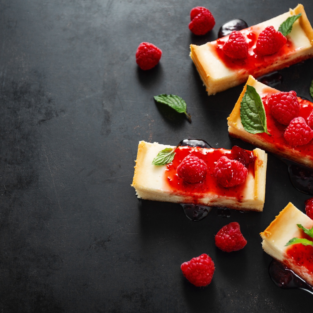 Pieces of cheesecake on a table with jam and raspberries