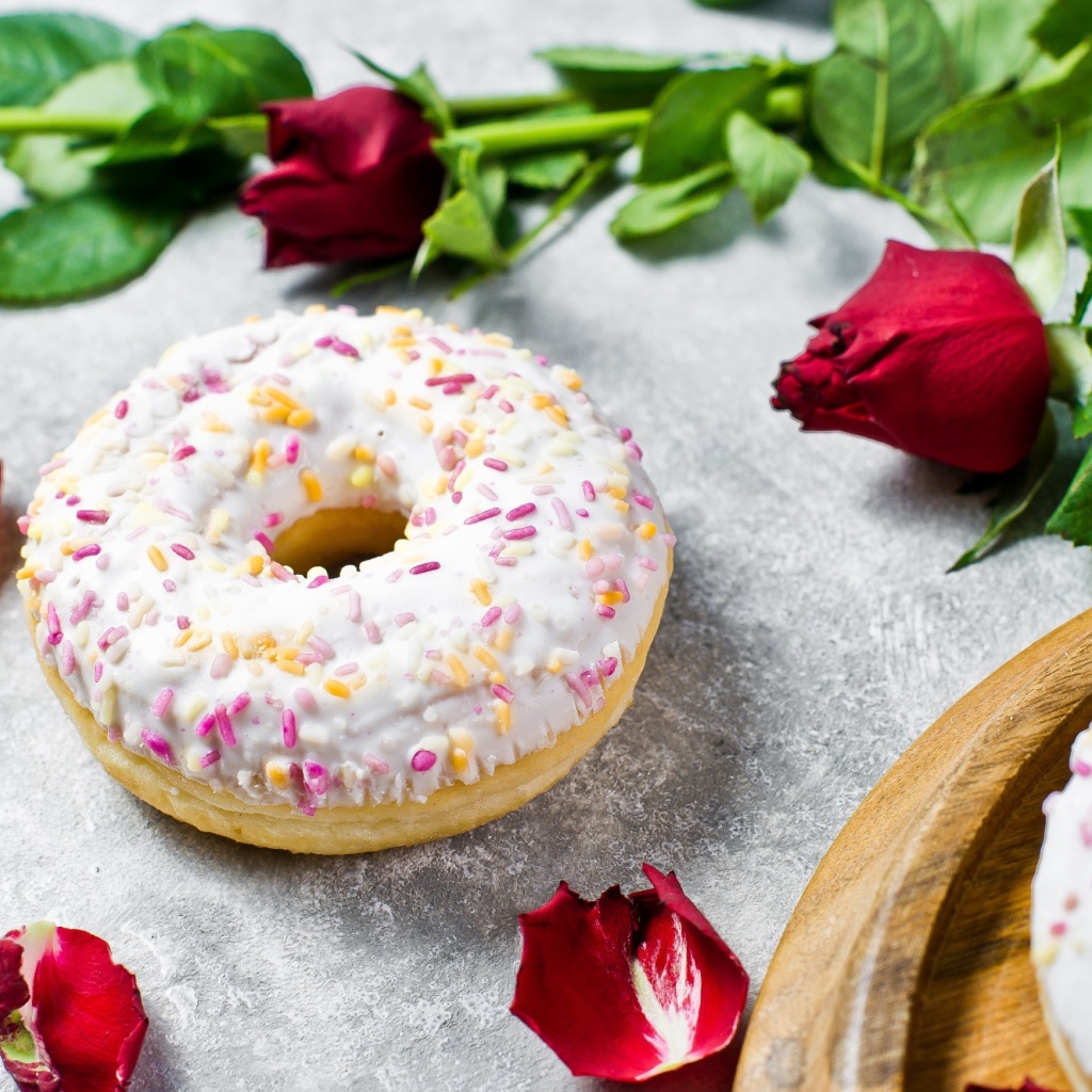 Сладкий пончик с глазурью на столе с красными розами