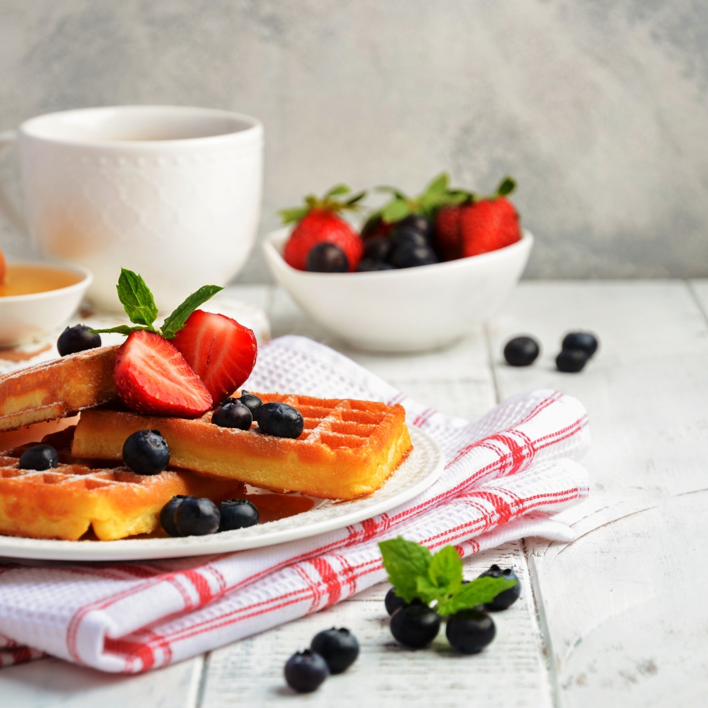 Сладкие вафли с ягодами черники и клубники на столе с медом и чаем