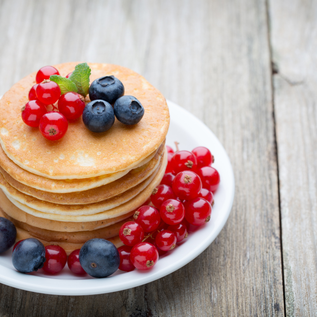 Вкусные оладьи на тарелке с ягодами красной смородины и черники