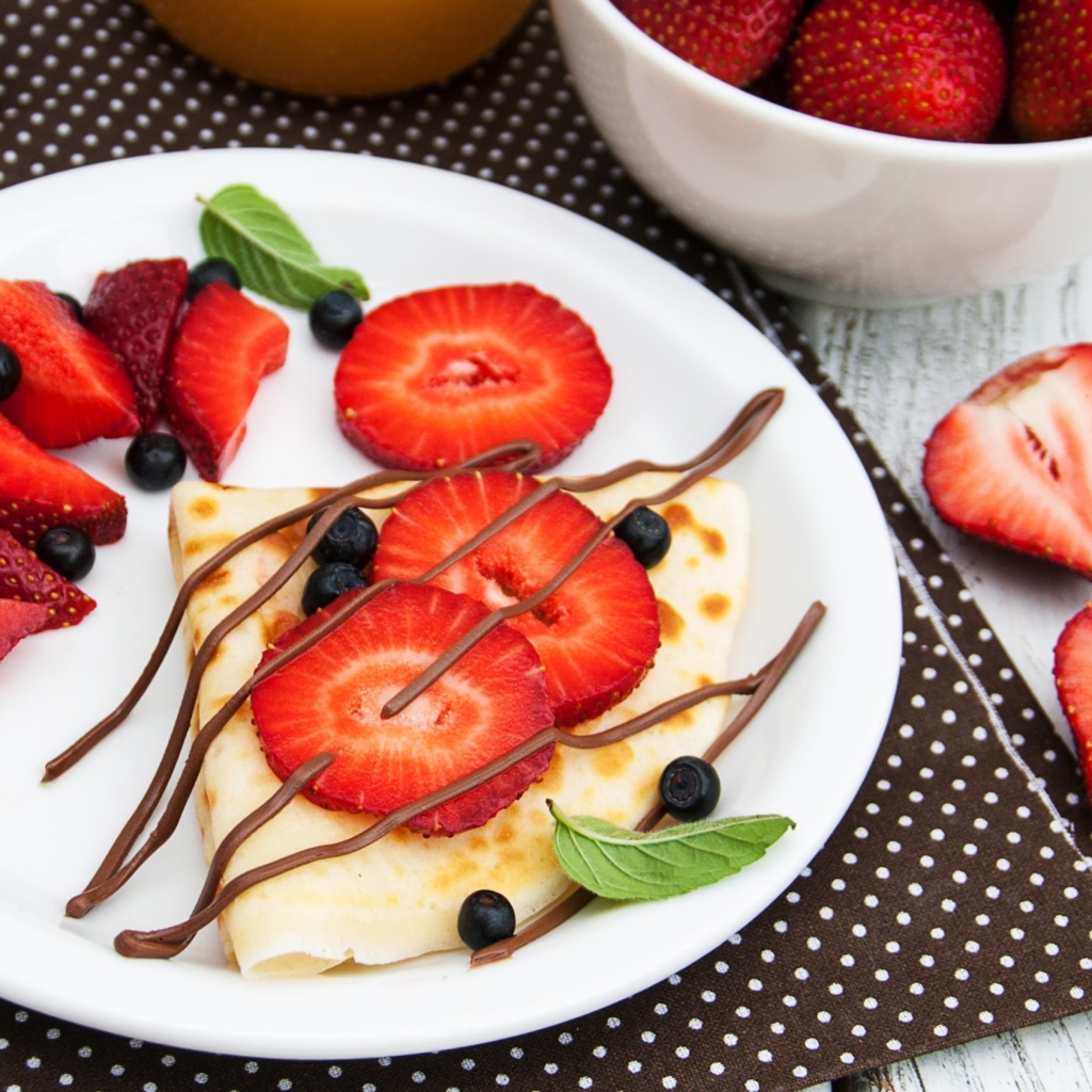 Тонкий блинчик на тарелке с шоколадом, ягодами клубники и черники