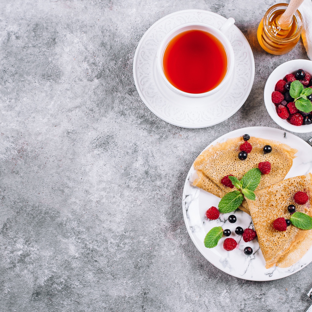 Тонкие блинчики на столе с ягодами, чаем и медом