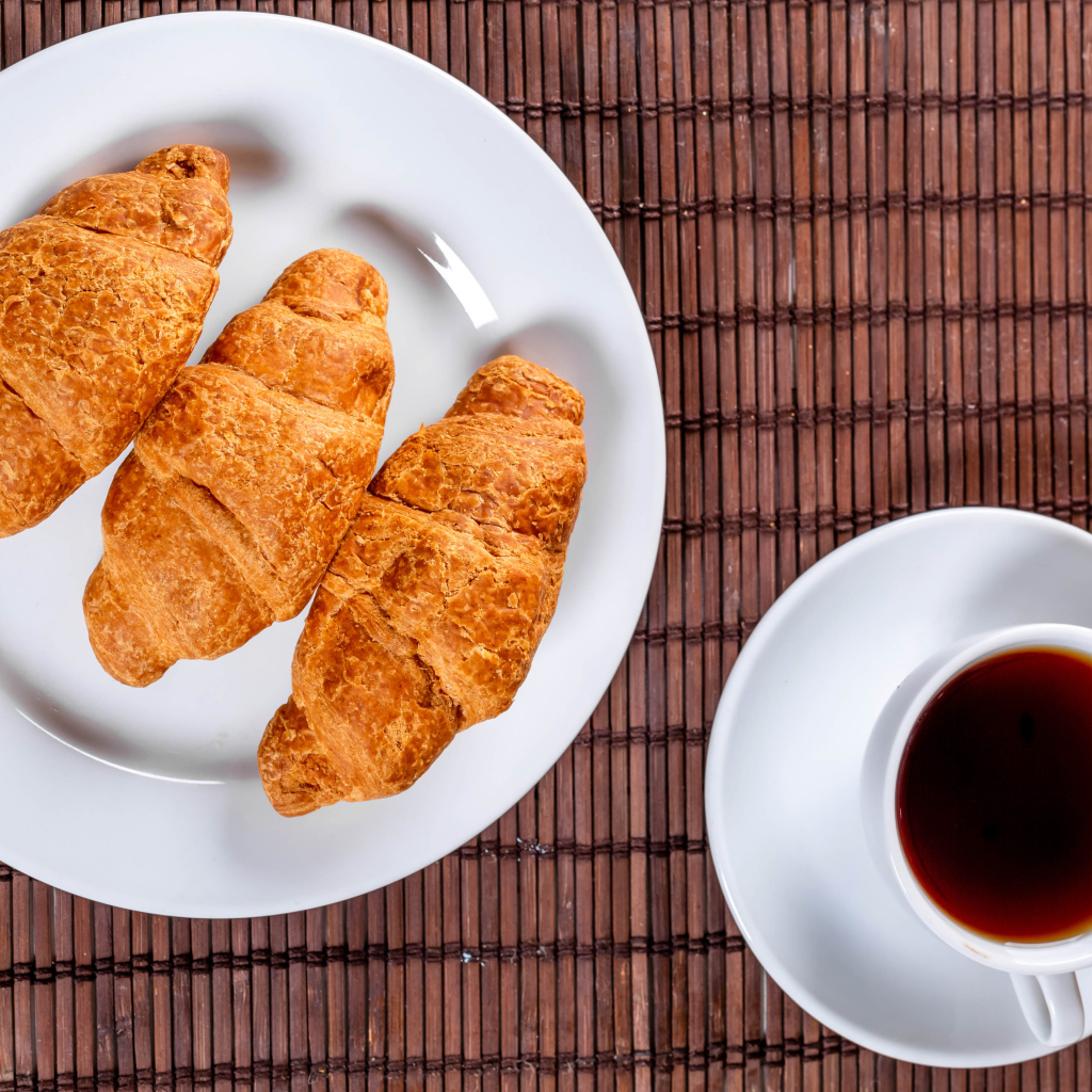 Три круассана на белой тарелке на столе с чаем