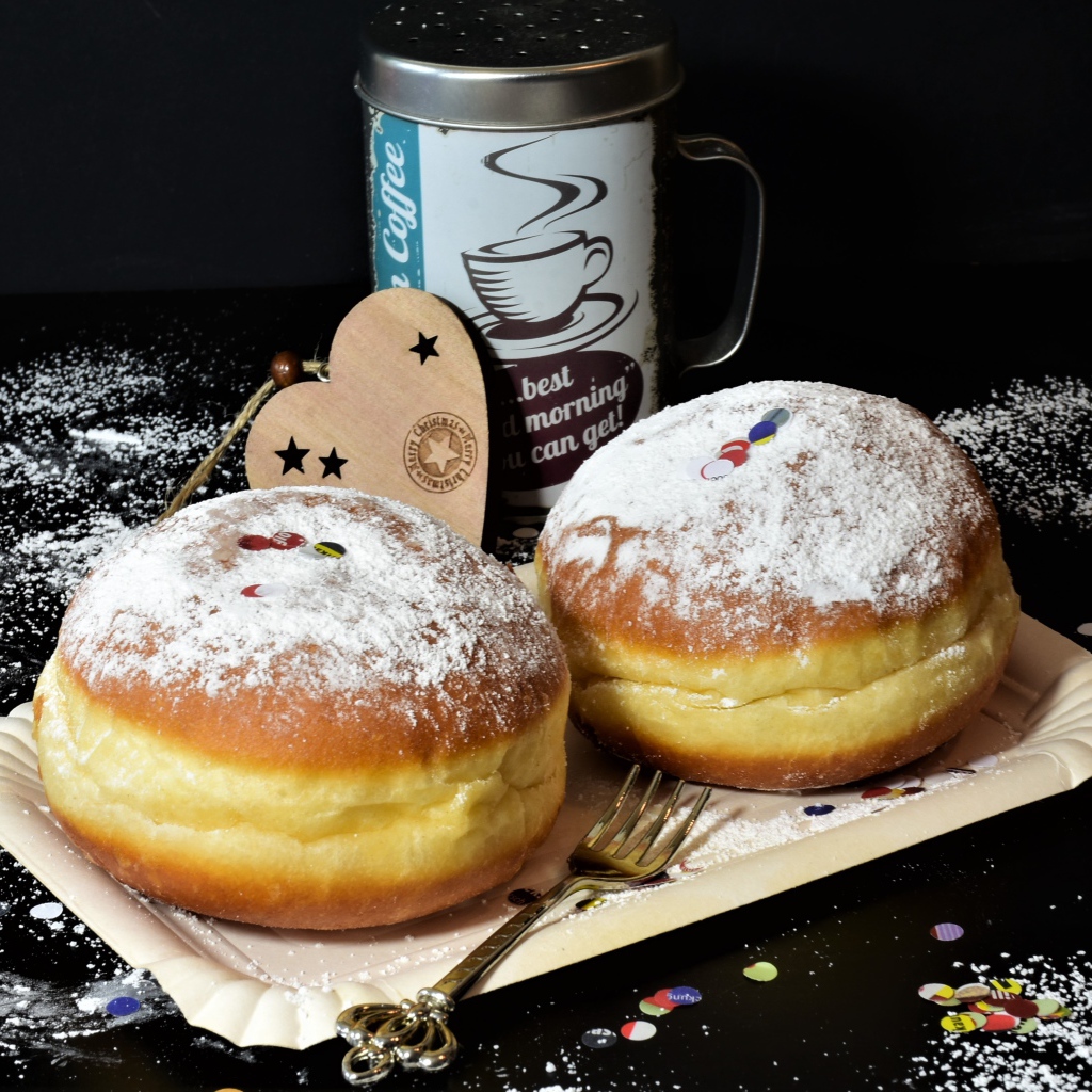 Два пышных пончика с сахарной пудрой на черном столе с кофе
