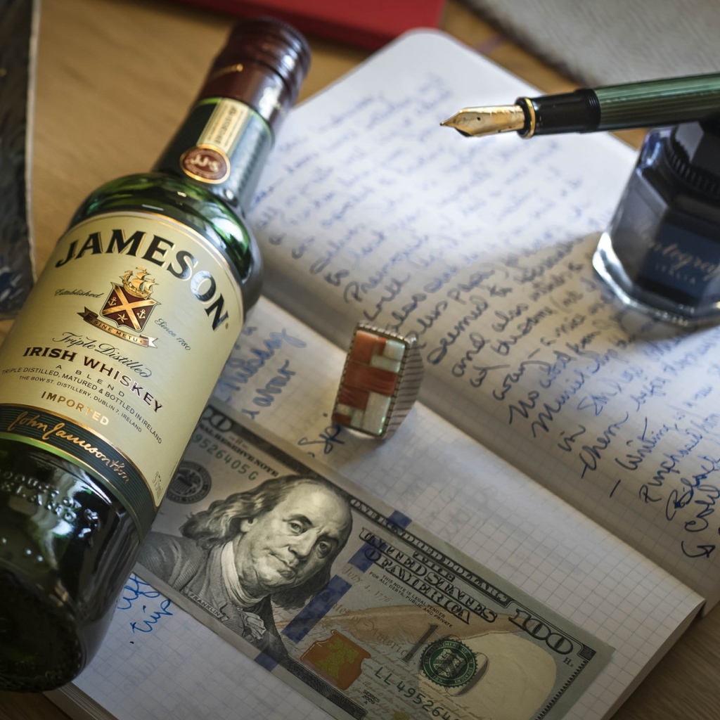 Бутылка виски лежит на тетради с чернильницей и купюрой