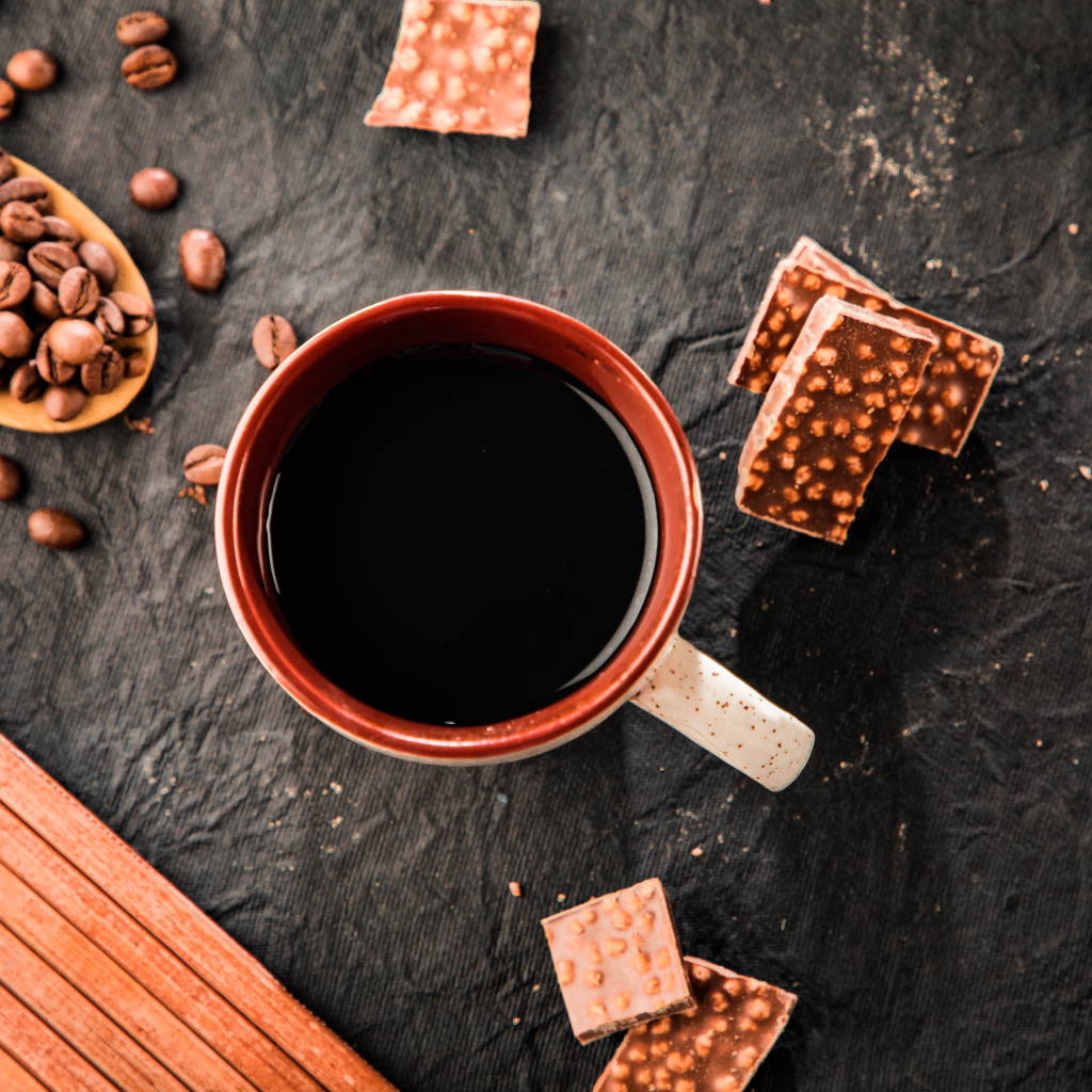 Чашка кофе на столе с кусочками шоколада и кофейными зернами