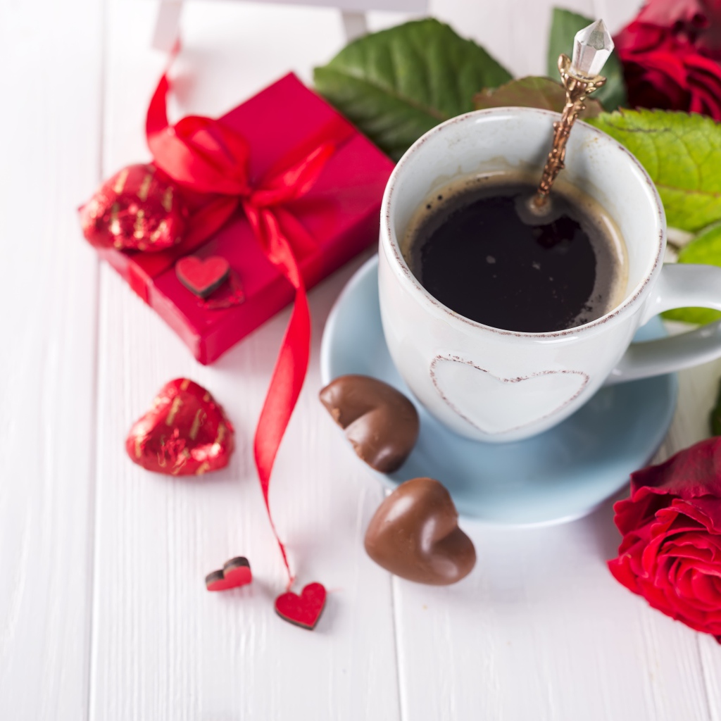 Чашка кофе на столе с шоколадными конфетами, подарком и красной розой