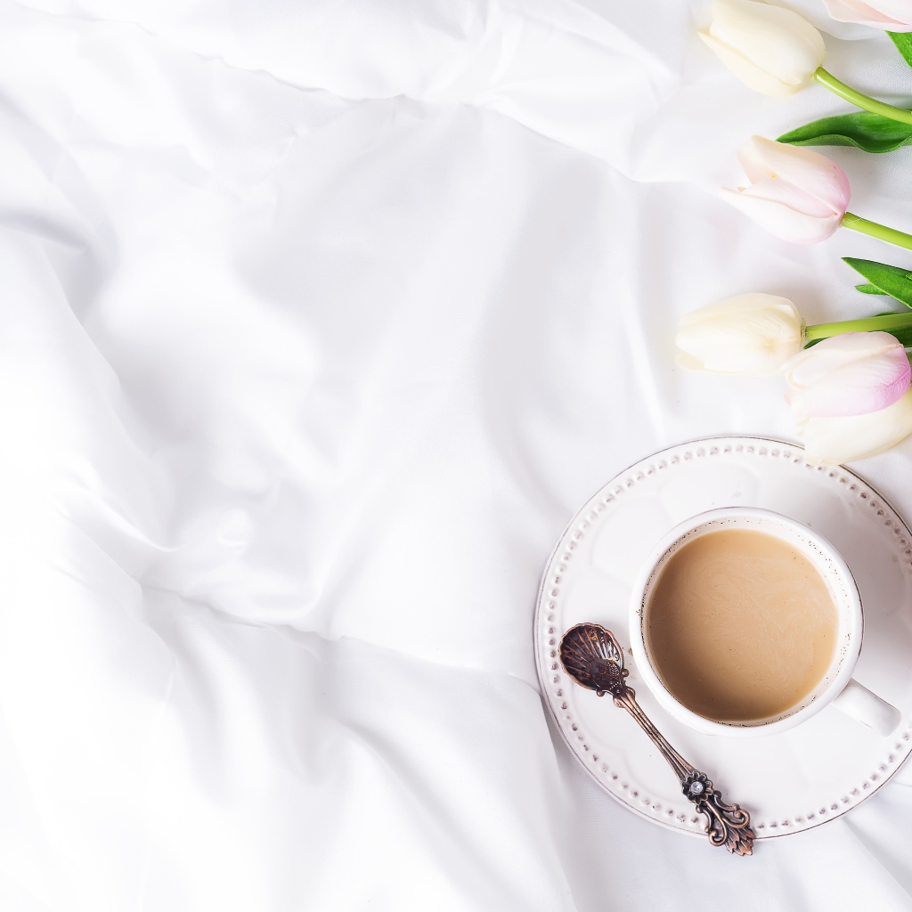 Чашка кофе на белом покрывале с тюльпанами