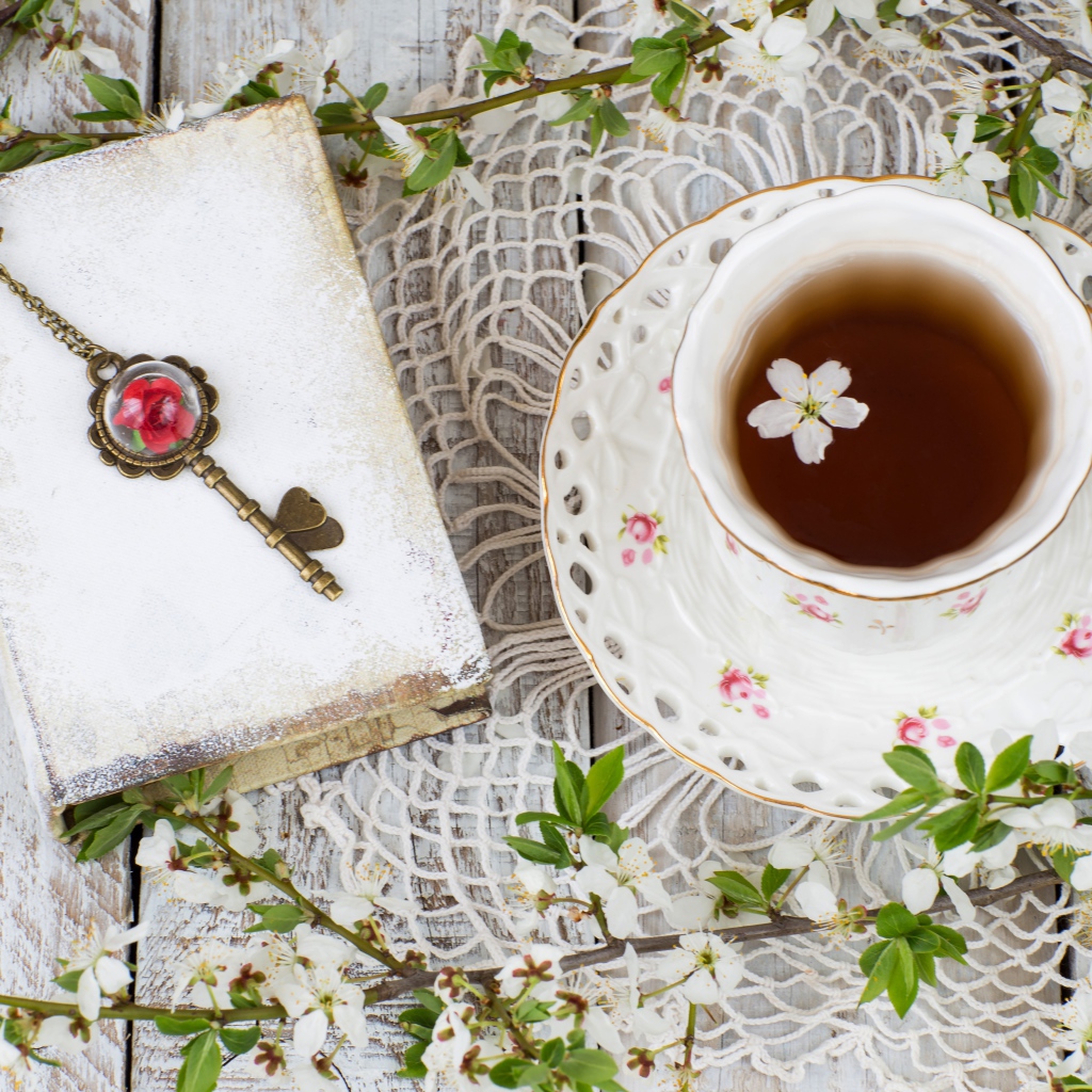 Чашка чая на столе с книгой и белыми цветами вишни 
