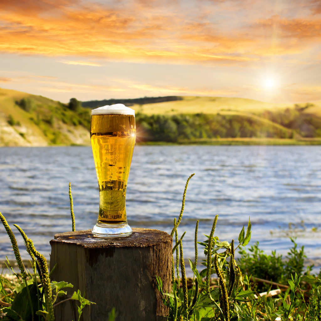 Бокал пива стоит на пне у воды 