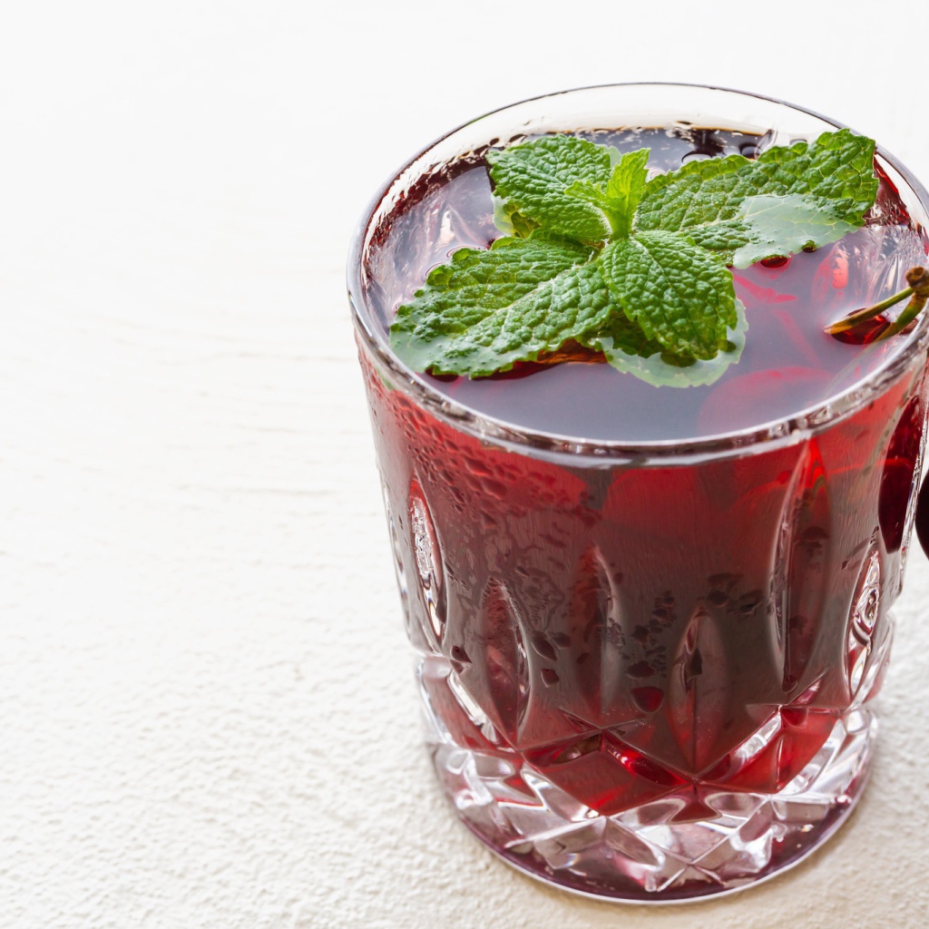 Стакан вишневого сока с мятой на белом фоне