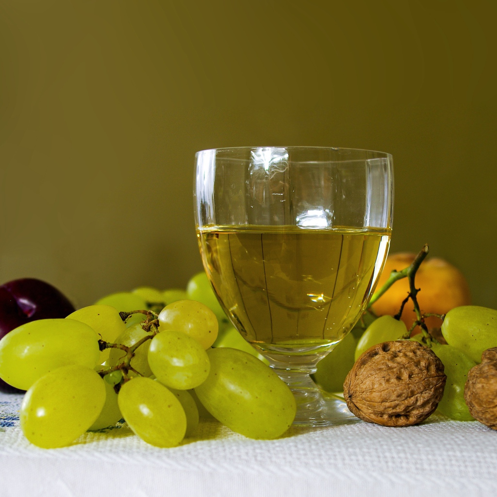 Бокал белого вина на столе с виноградом и орехами