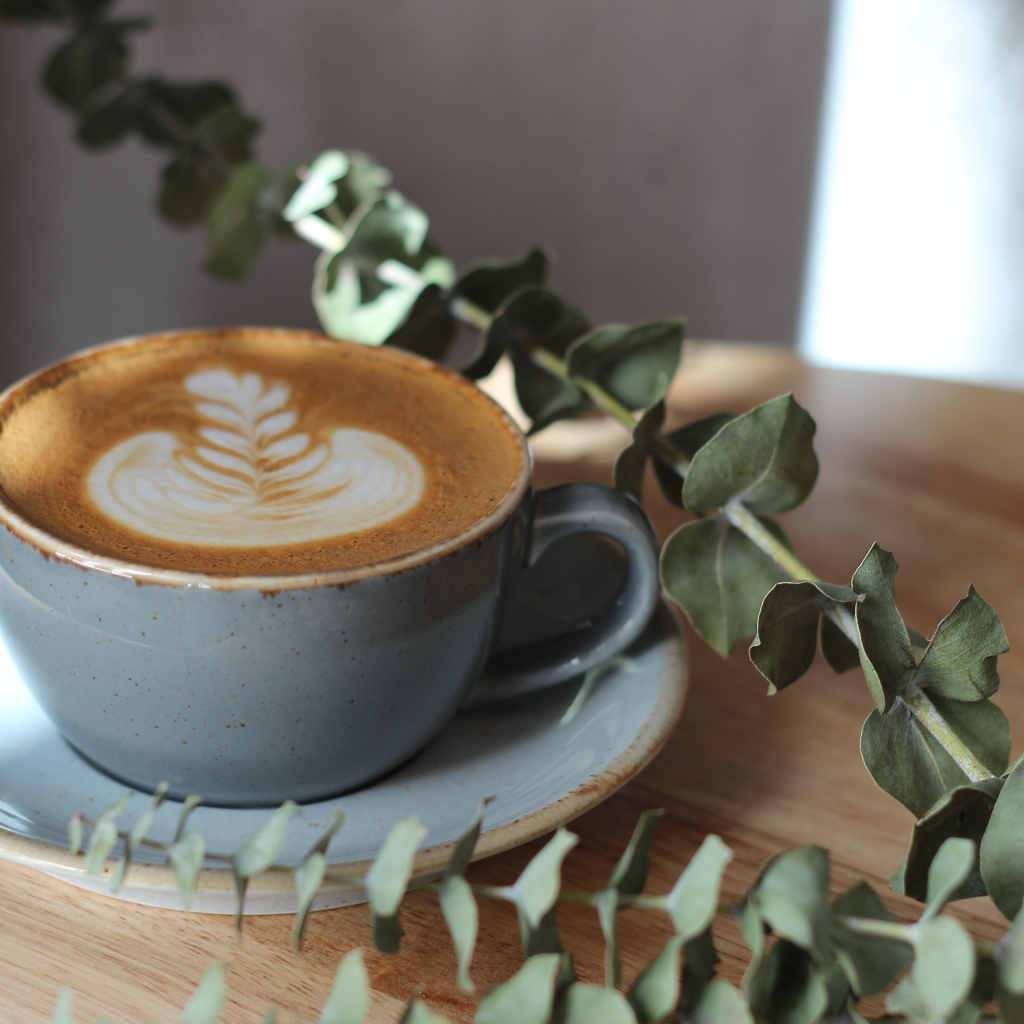 Большая чашка кофе с рисунком на пене на столе с веткой