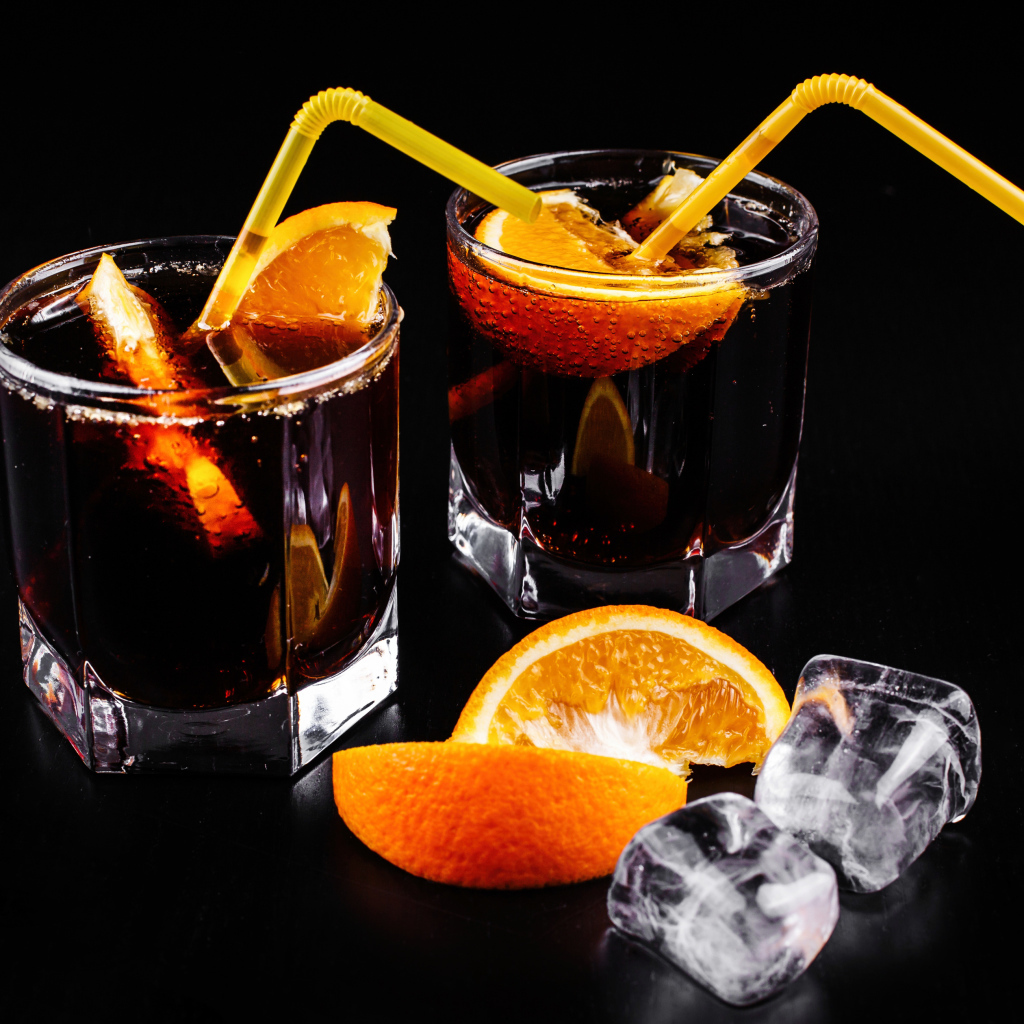 Коктейль с кусочками апельсина на черном фоне со льдом
