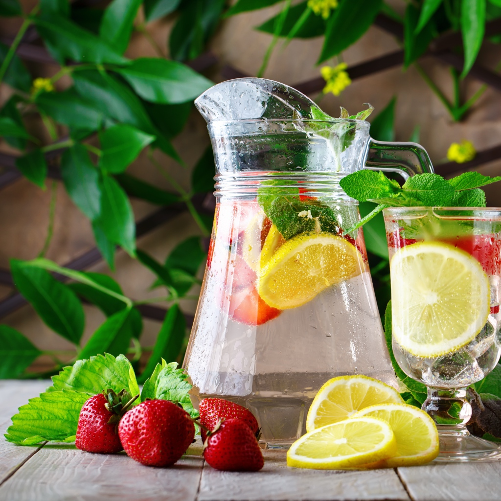 Холодный мохито в графине на столе с клубникой и лимоном