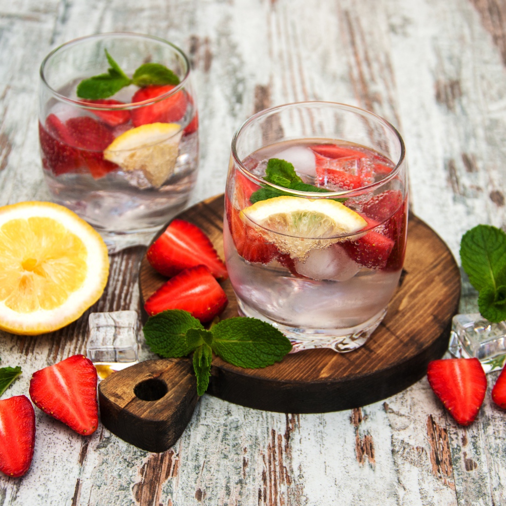 Холодный мохито на столе с ягодами клубники, лимоном и мятой