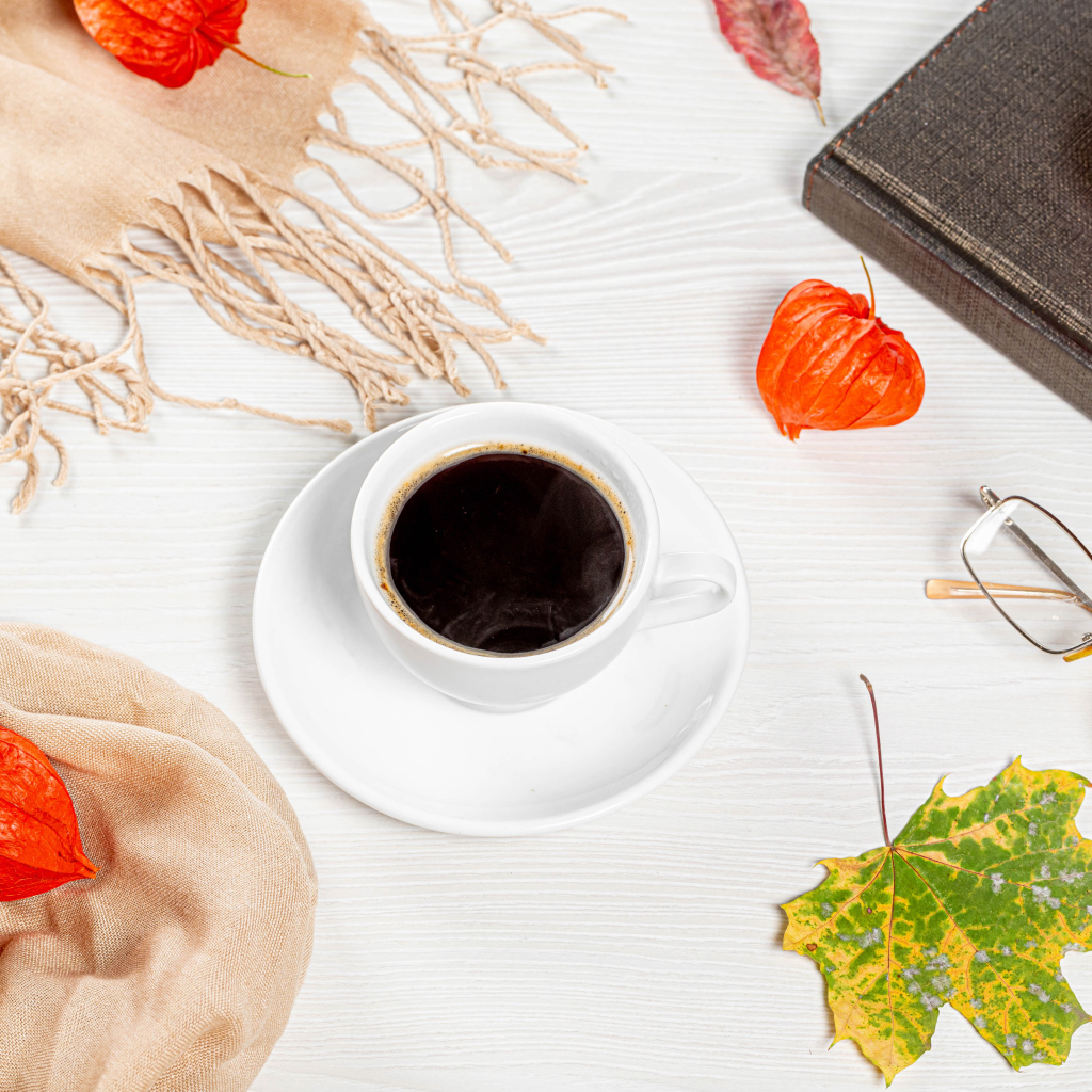 Чашка кофе на столе с книгой, очками и физалисом