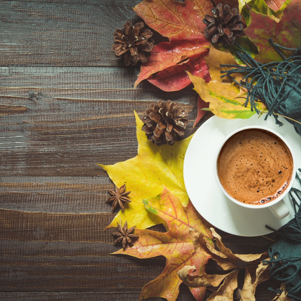 Чашка кофе на столе с шарфом, желтыми листьями и шишками