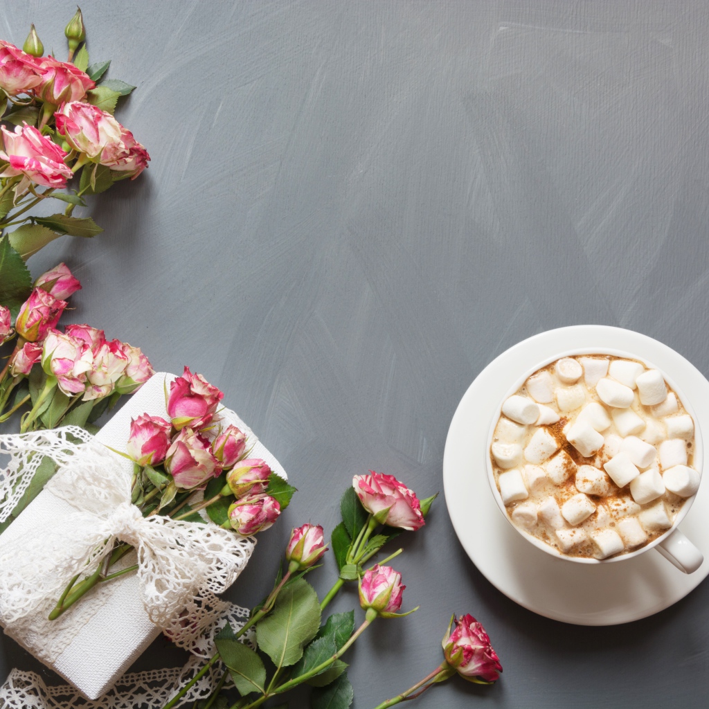 Чашка кофе с маршмеллоу на столе с подарком и букетом роз