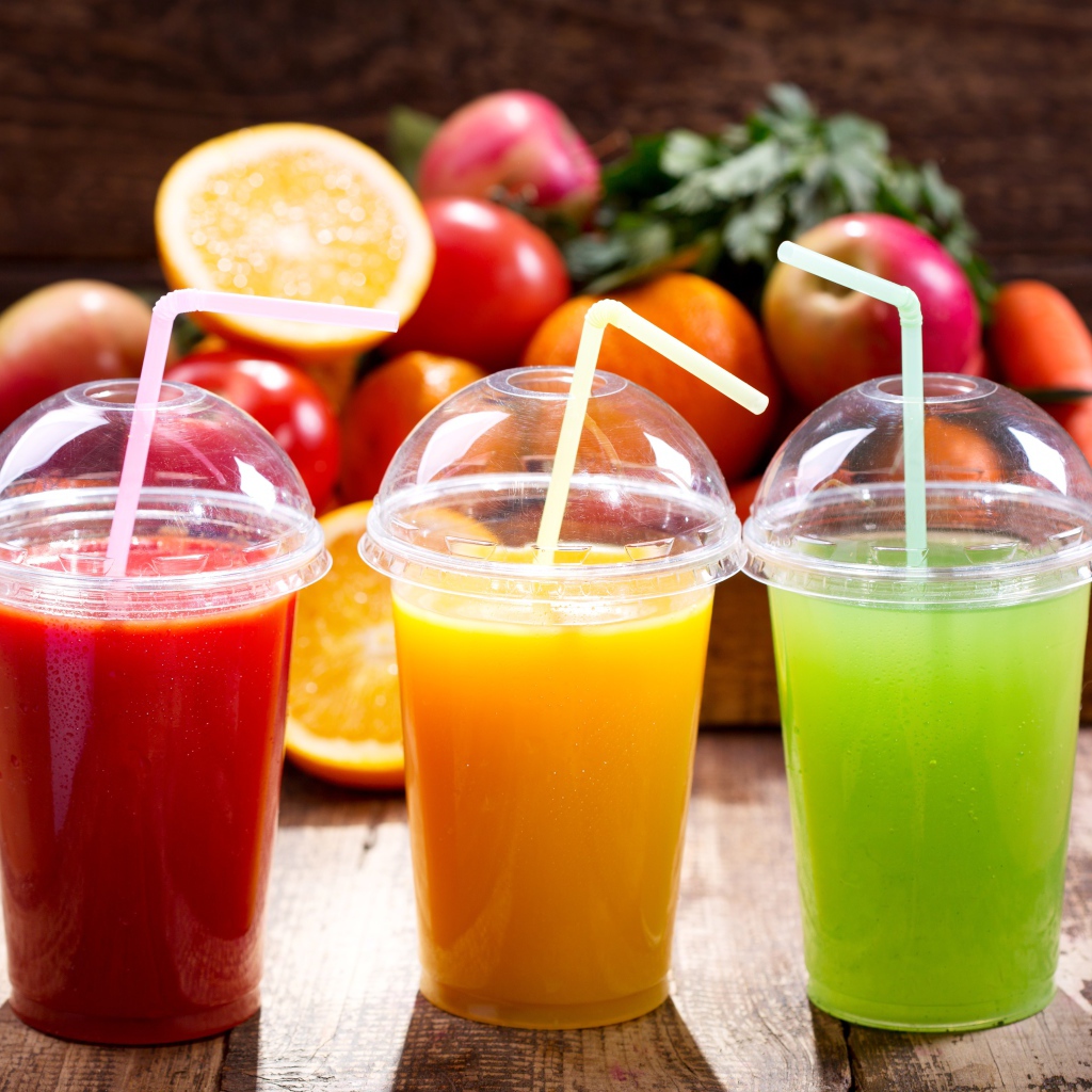 Свежие соки в стаканах с трубочками на столе