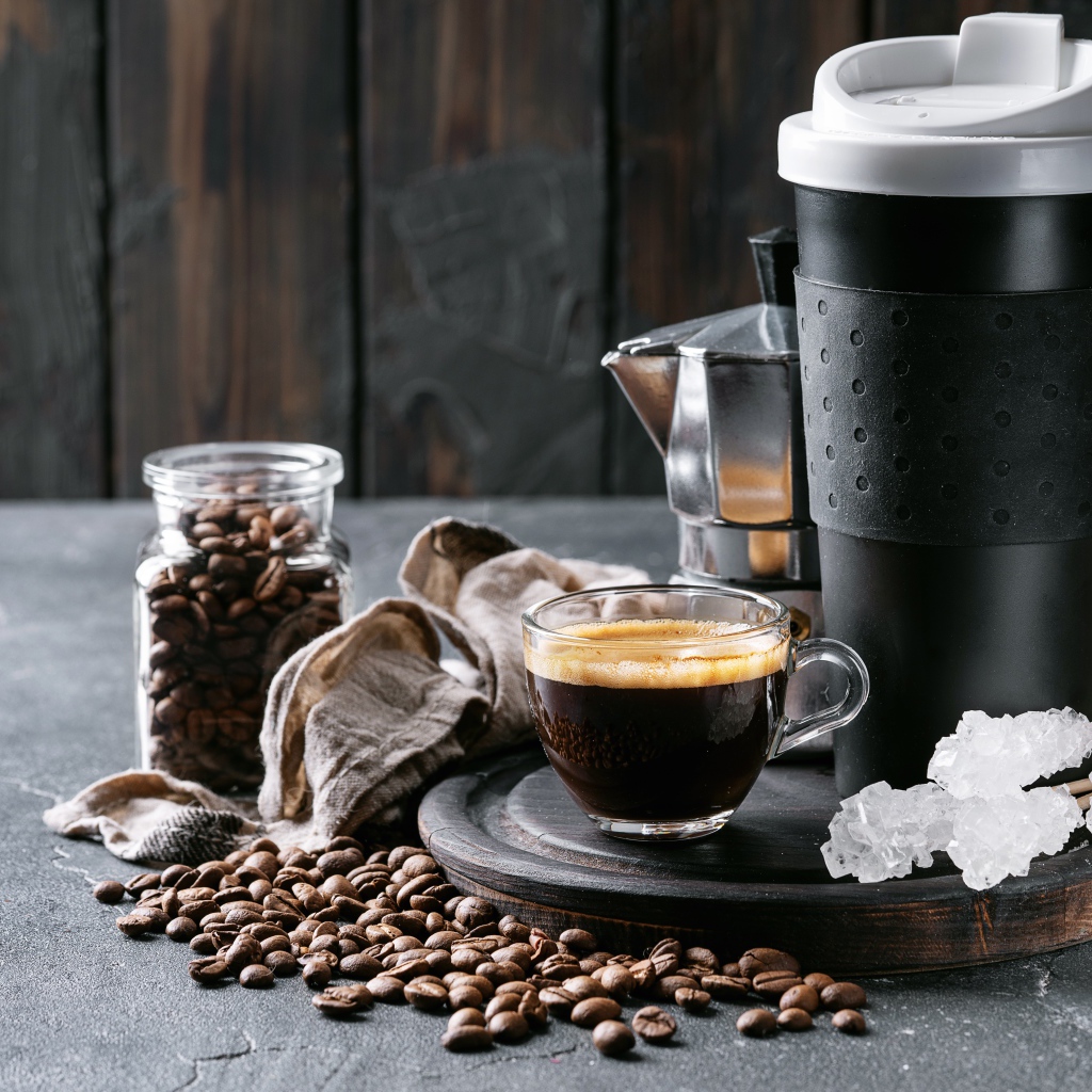 Стеклянная чашка кофе на столе с термосом и зернами