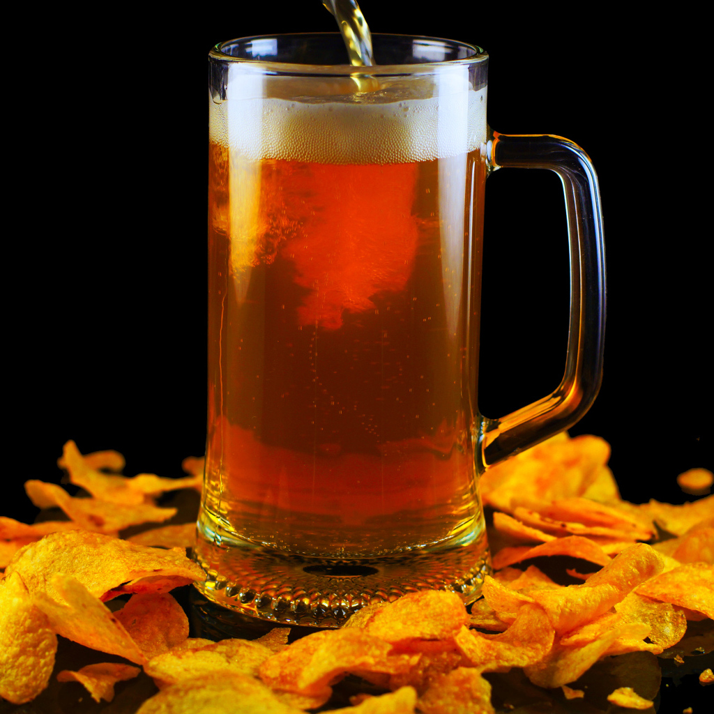 Бокал пива с чипсами на черном фоне