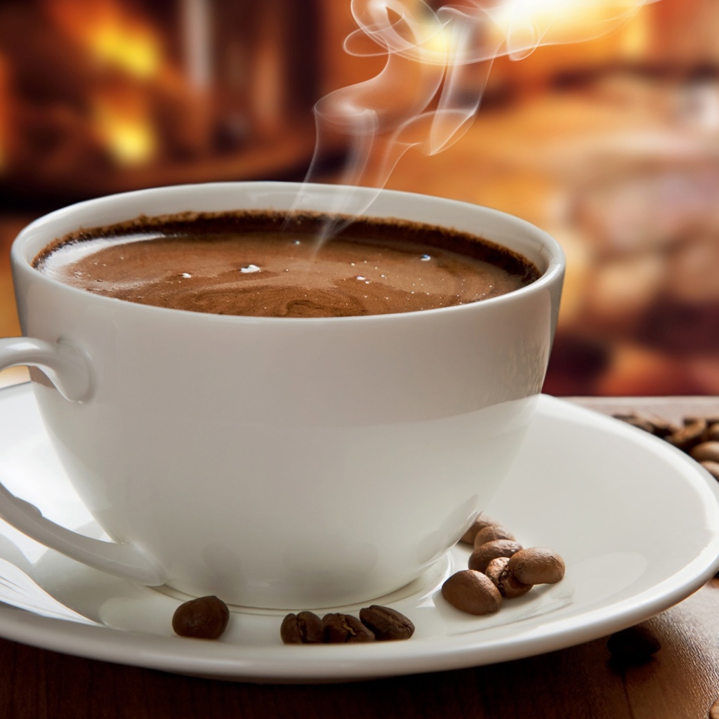 Большая белая чашка с горячим кофе на столе с кофейными зернами