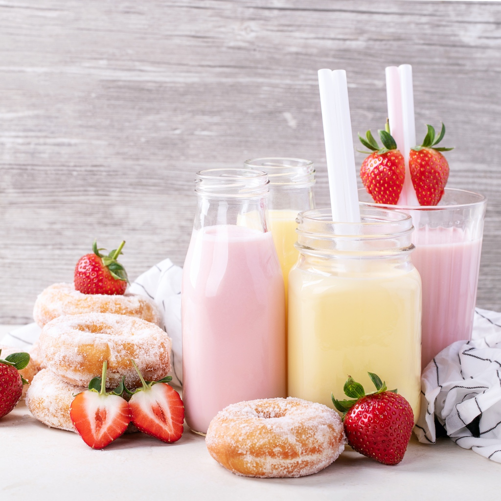 Молочные коктейли на столе с пончиками и ягодами клубники 