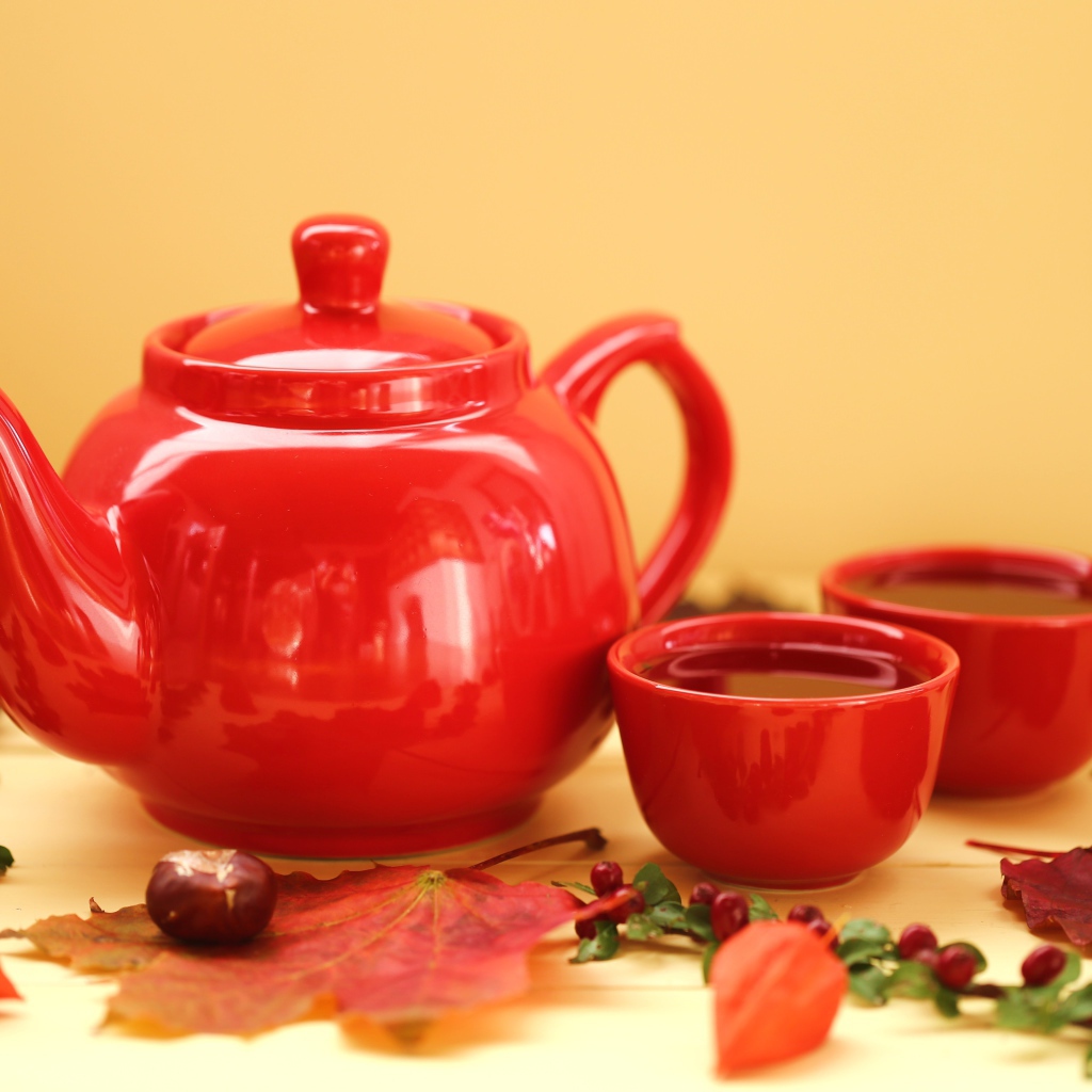 Красный чайник с чашками на столе осенью 