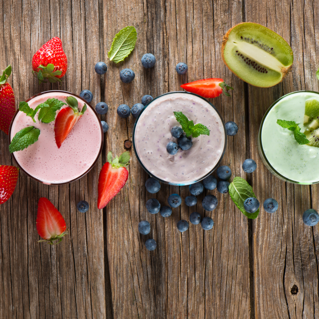 Стаканы со смузи на столе с киви, ягодами клубники и черники