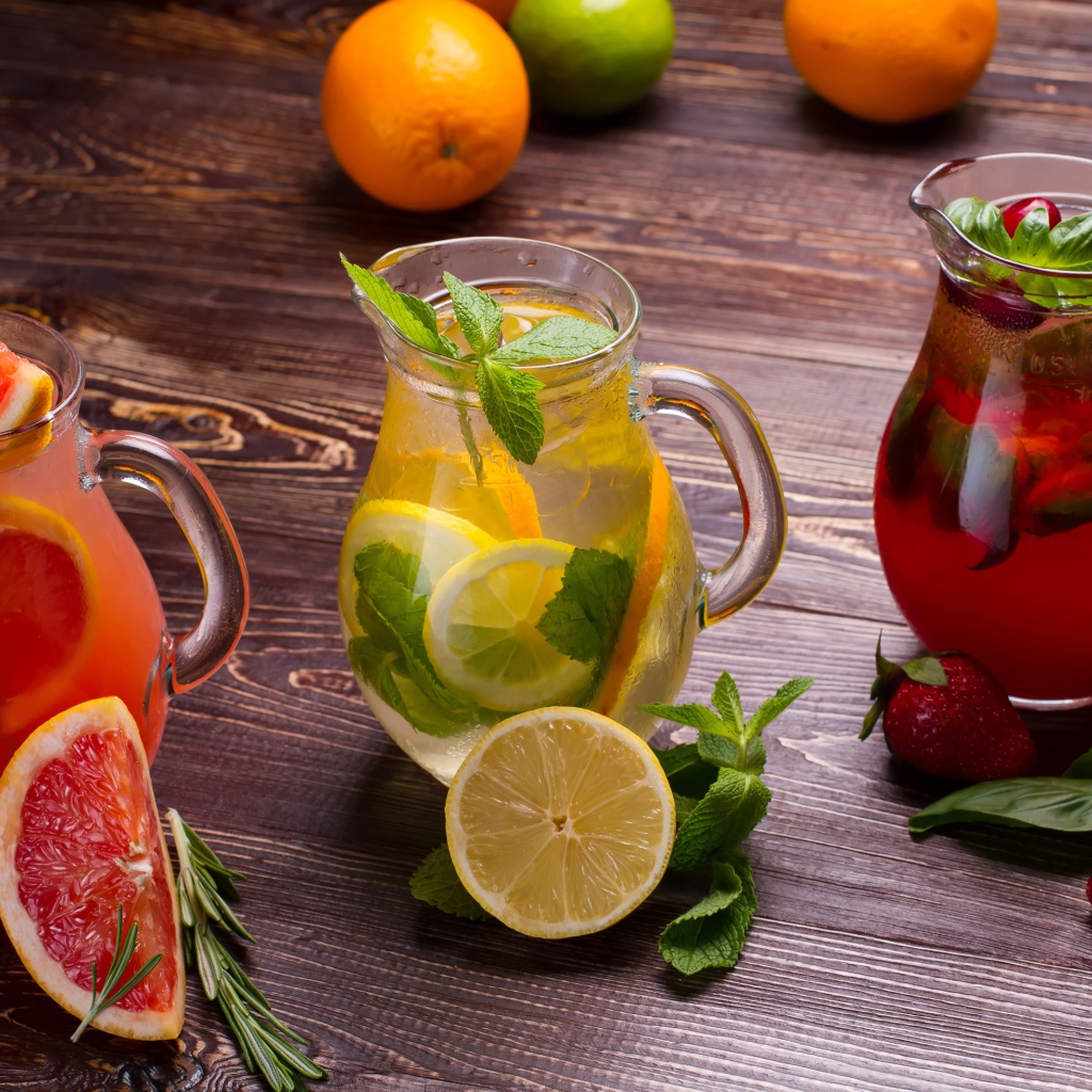 Три стеклянных графина с напитком на деревянном столе с фруктами