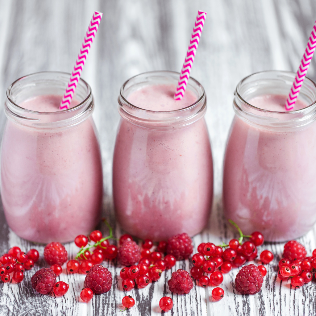 Три банки ягодного  смузи на столе с ягодами малины и смородины