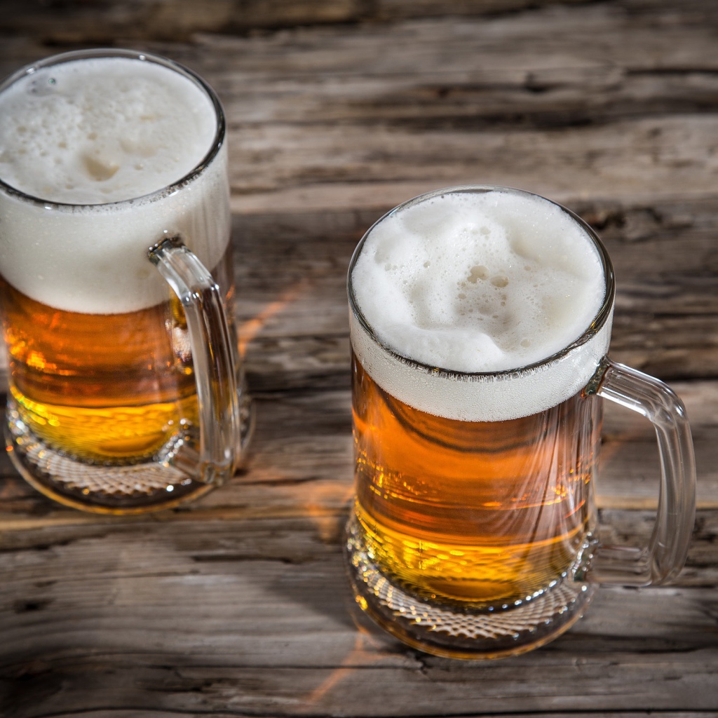 Два бокала пива с пеной на деревянном столе