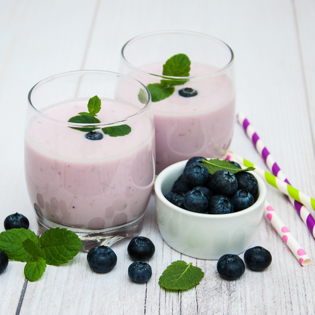 Два стакана коктейля в стаканах на столе с ягодами черники и трубочками