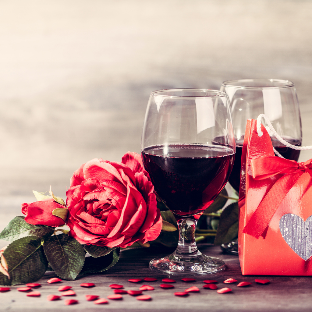 Два бокала красного вина на столе с розой и подарком 
