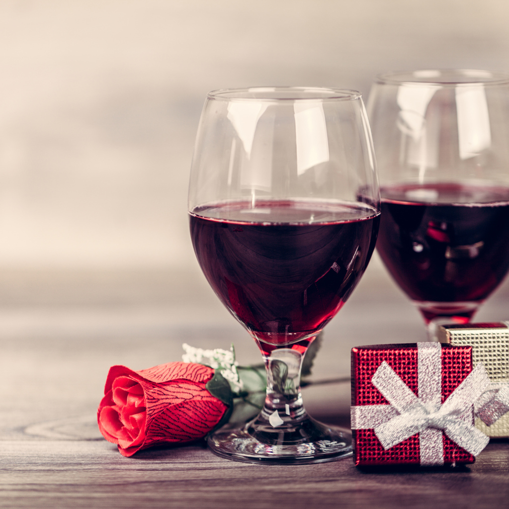 Два бокала вина на столе с подарками и красной розы 