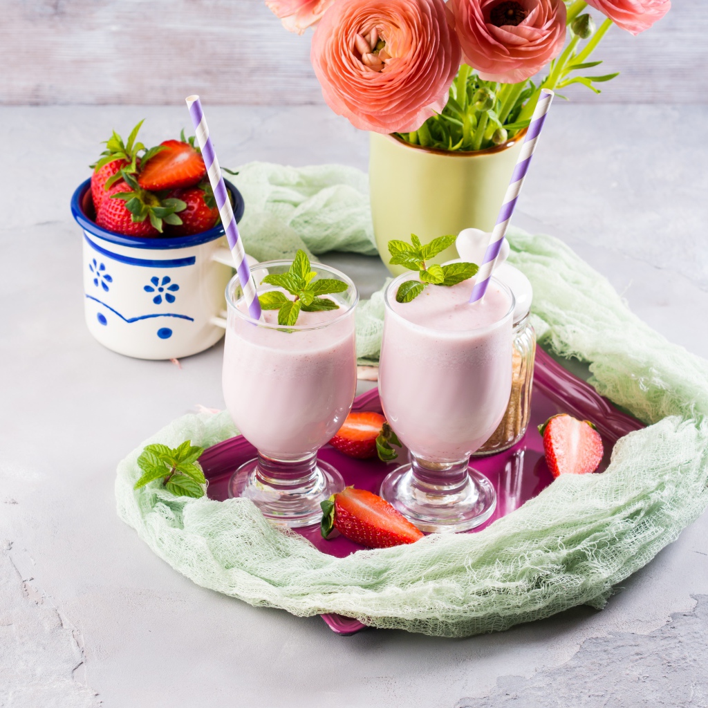 Два стакана с коктейлем на столе с букетом и клубникой