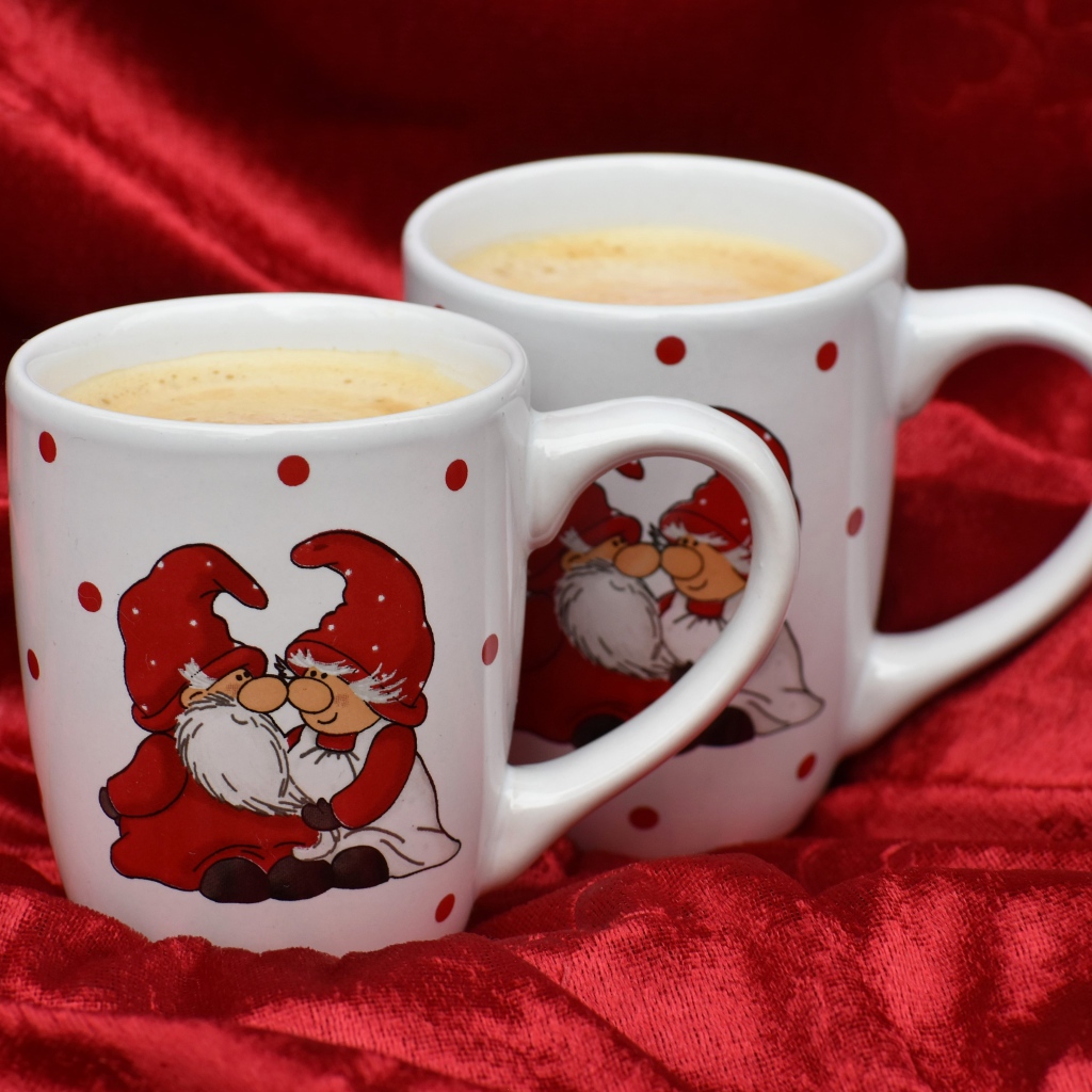 Две белые чашки кофе с рисунком стоят на красной ткани