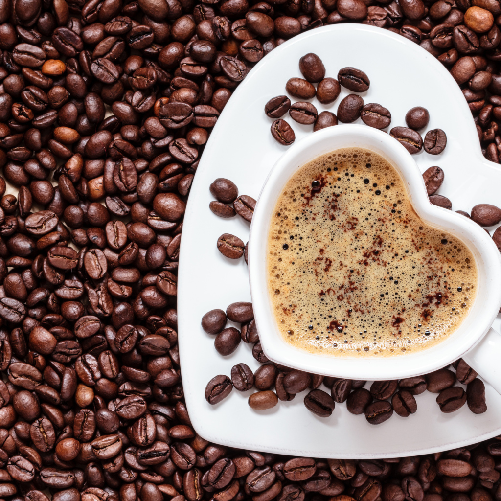 Белая чашка в форме сердца стоит на кофейных зернах 