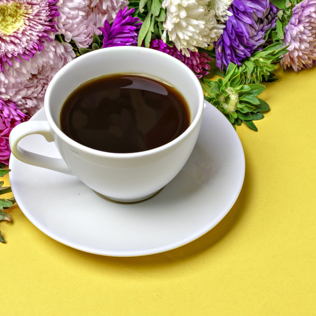 Белая чашка кофе на желтом фоне с букетом цветов астры