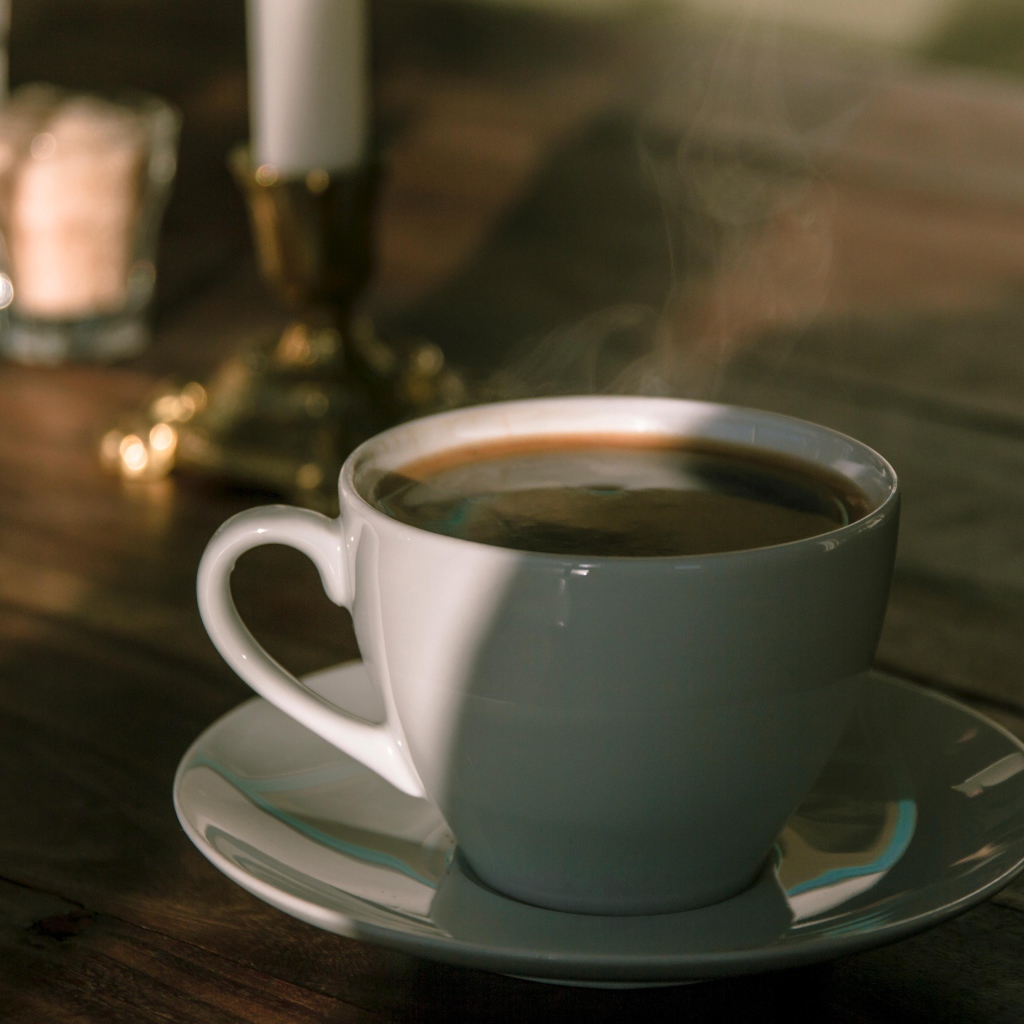 Белая чашка кофе на столе в лучах солнца