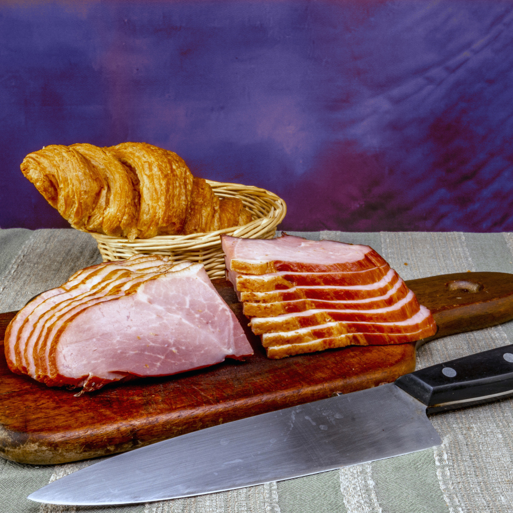 Кусок нарезанной ветчины на доске с круассаном