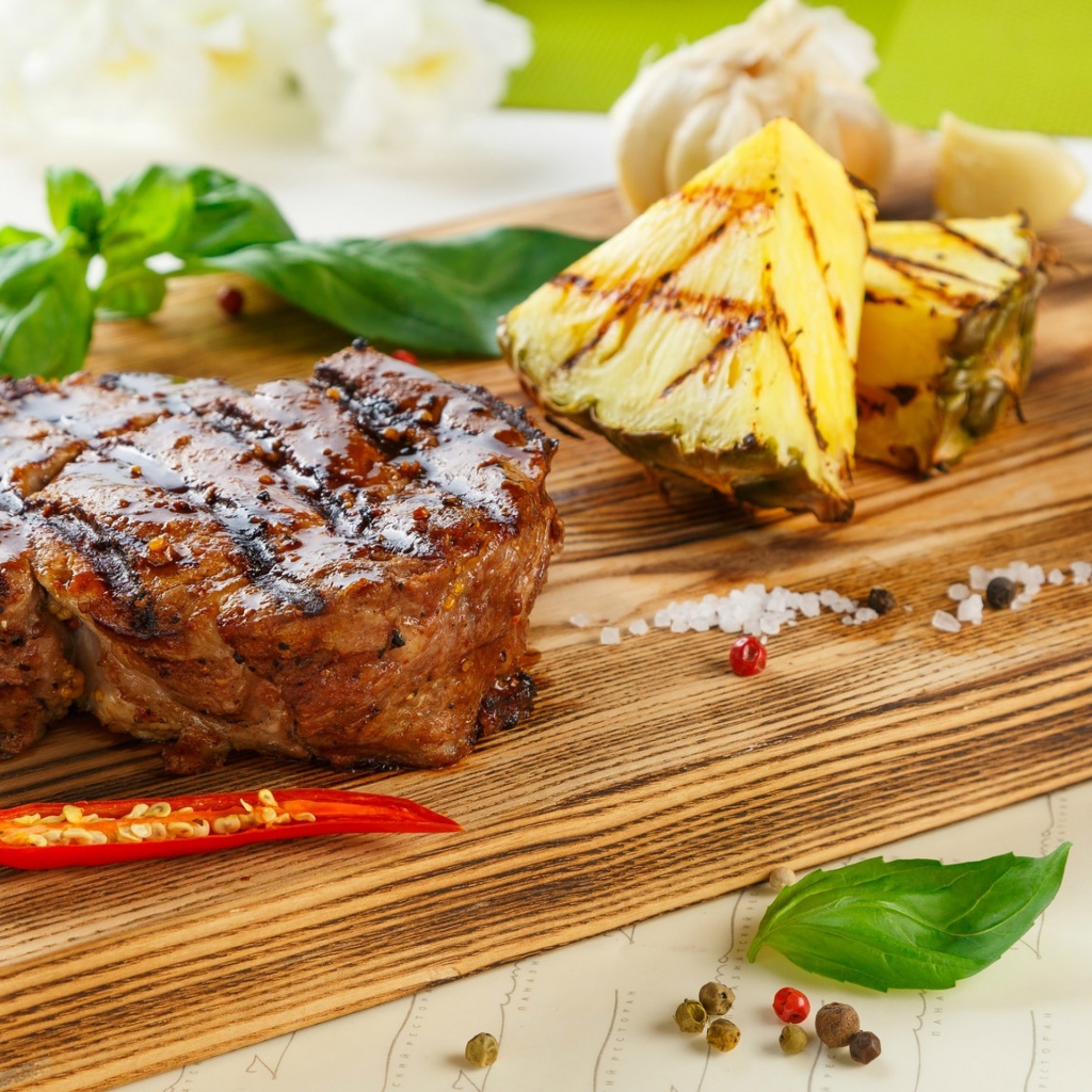 Кусок мяса гриль на деревянной доске с кусочками ананаса и базиликом
