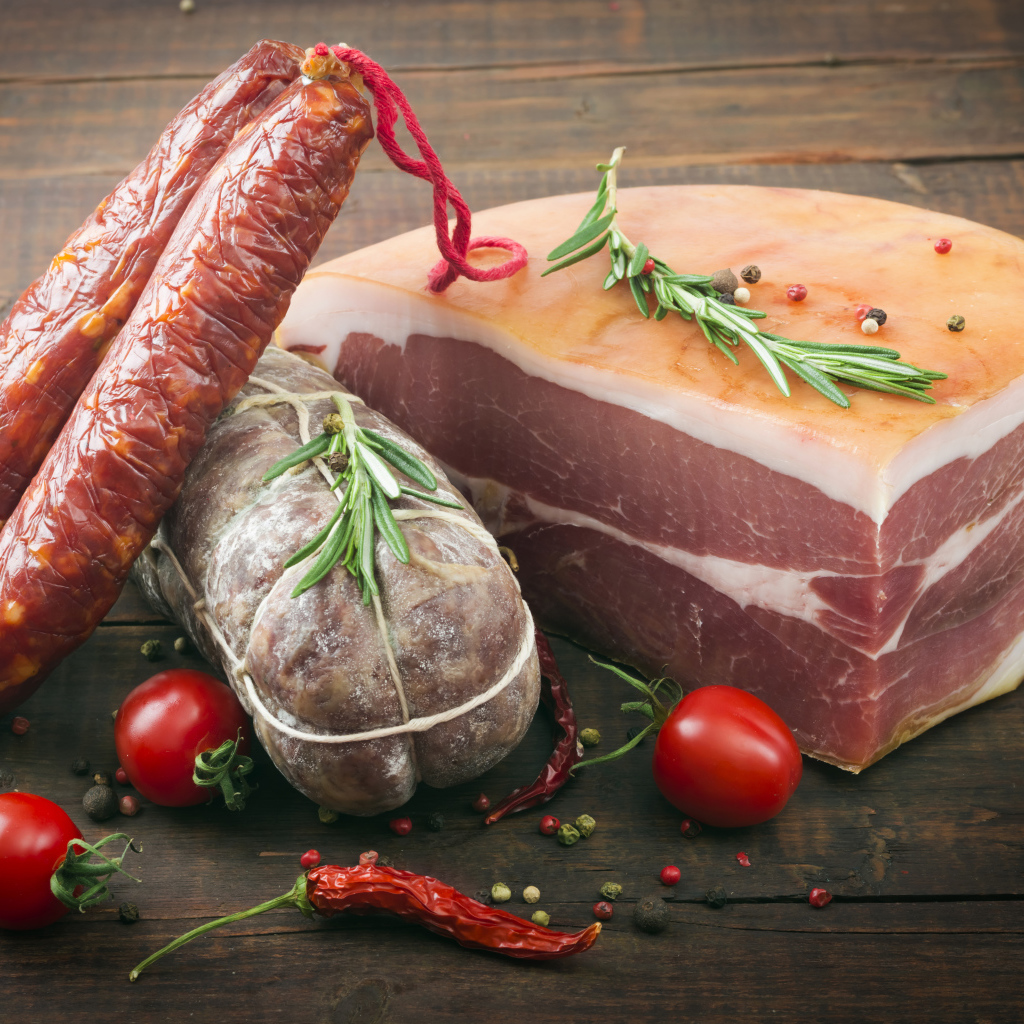 Кусок мяса и колбаса на деревянном столе с помидорами и специями