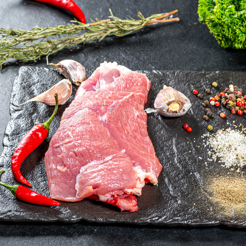 Кусок мяса на столе с острым перцем, чесноком и зеленью